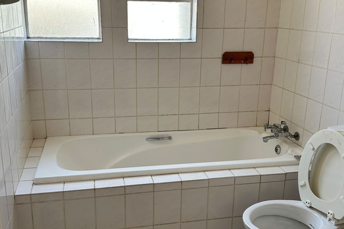 A dated bathroom featuring a built-in bathtub, ceramic wall tiling, and a standard toilet, requiring cosmetic updates to improve its overall condition.