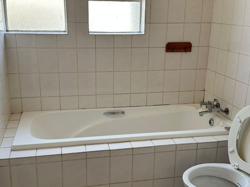 A dated bathroom featuring a built-in bathtub, ceramic wall tiling, and a standard toilet, requiring cosmetic updates to improve its overall condition.