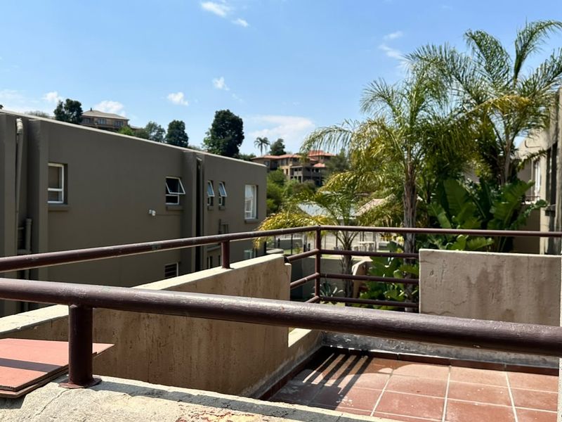 An open-air balcony featuring tiled flooring, a metal safety railing, and a concrete parapet wall with views of the surrounding residential complex.