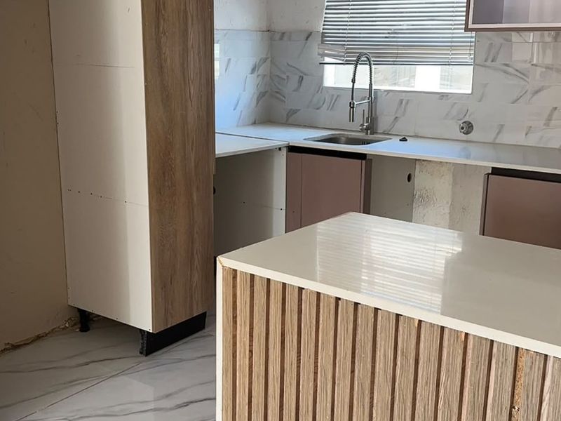 An unfinished kitchen space featuring modern marble-look tiling, quartz countertops, and wood-veneer cabinetry, currently awaiting final installation and completion of finishes.