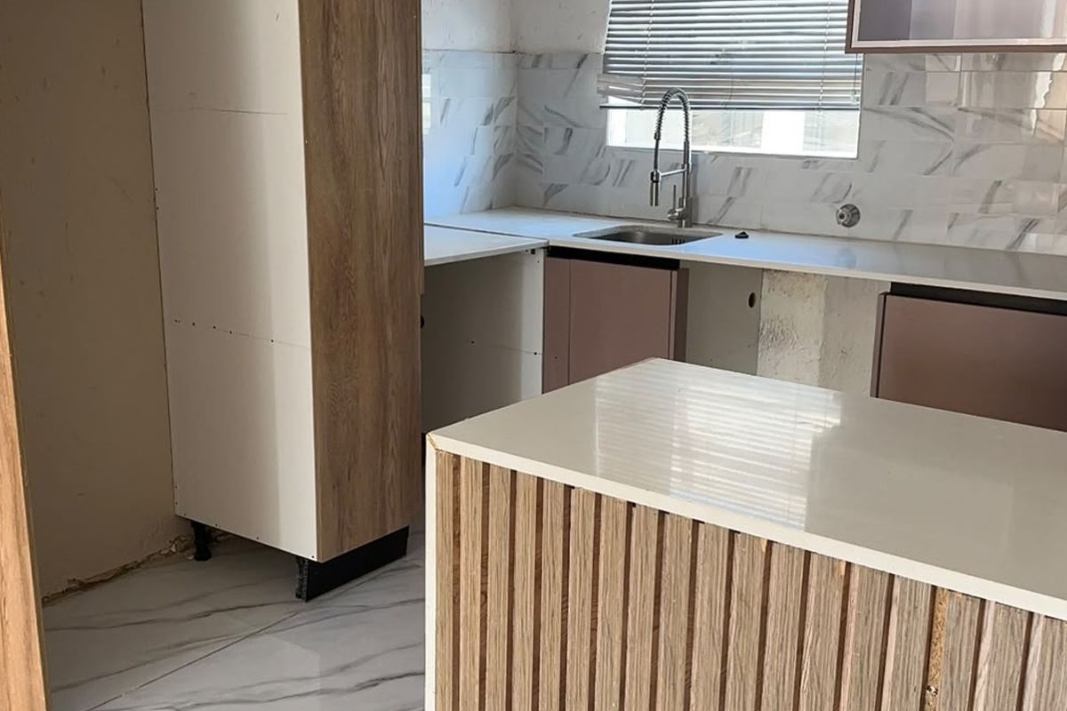 An unfinished kitchen space featuring modern marble-look tiling, quartz countertops, and wood-veneer cabinetry, currently awaiting final installation and completion of finishes.