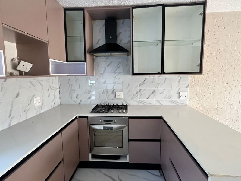 Modern kitchen featuring sleek mauve cabinetry, white quartz countertops, marble-look tiled backsplash, and integrated stainless steel oven and gas hob.