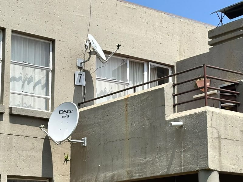 Exterior view of an apartment building facade featuring a balcony, concrete wall finish, and satellite dish installations.