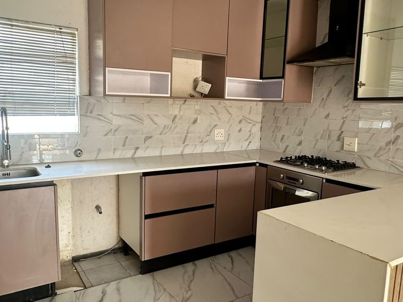 A kitchen featuring built-in cabinetry, stone countertops, a gas hob, and an oven, currently requiring finishing touches to the base cabinetry and wall areas.