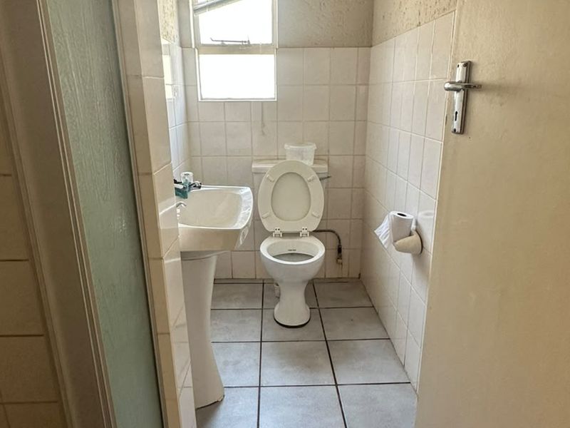 A compact bathroom featuring a pedestal basin, toilet, and tiled finishes. The space is dated and would benefit from modern updates.