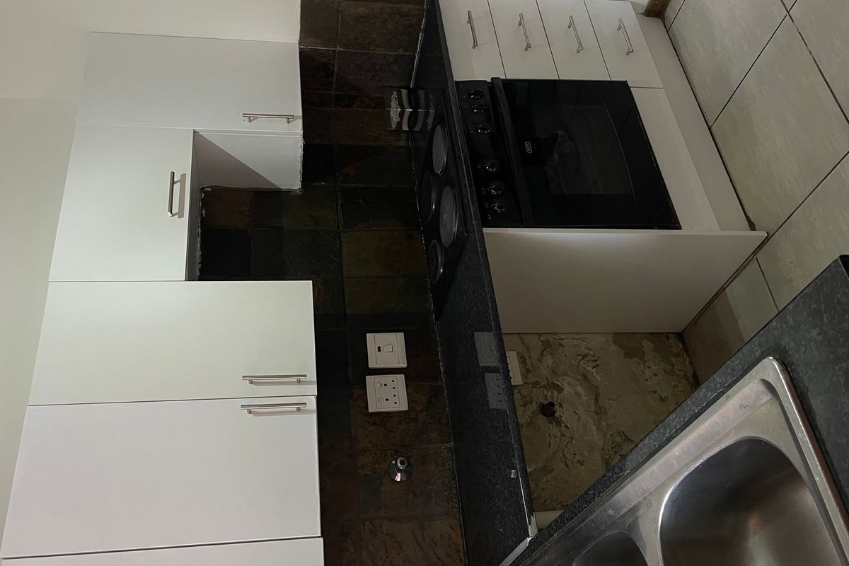 A compact kitchen featuring white cabinetry, a built-in oven and hob, and a stainless steel sink, currently requiring minor repairs and finishing.