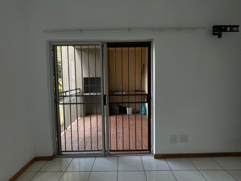 An empty living room featuring tiled floors, a sliding door with security gate, and access to a balcony area.