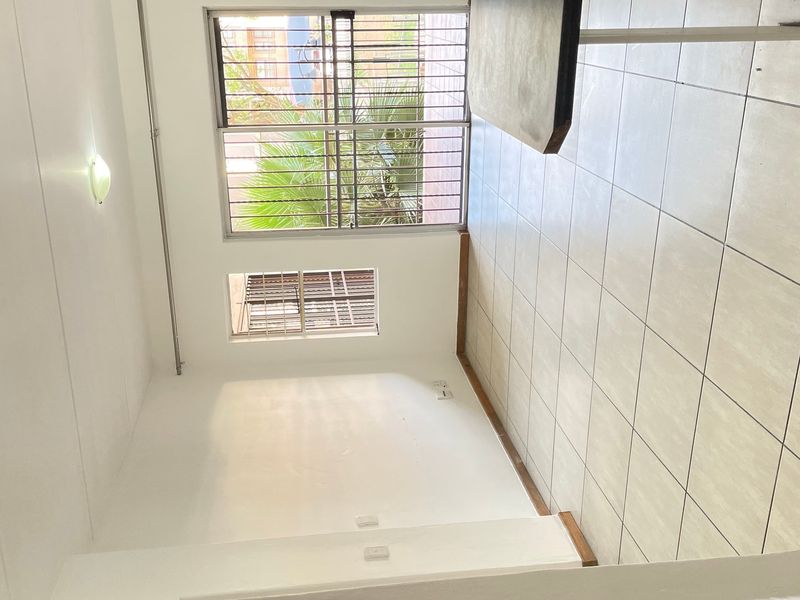 A bright, empty living area featuring neutral tiled flooring, security bars on windows, and a sliding door leading to the exterior.
