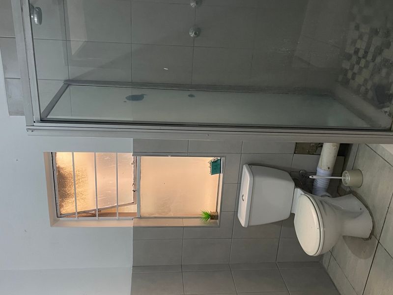 A functional bathroom featuring a shower enclosure, toilet, and tiled finishes, currently requiring maintenance to address exposed plumbing and wall damage.