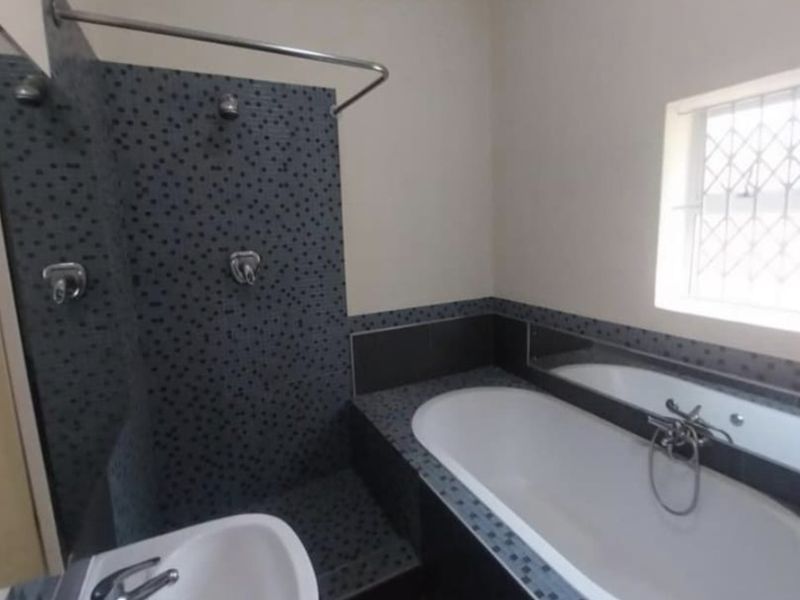 A functional bathroom featuring a built-in bathtub, shower area with mosaic tiling, and a basin, finished with neutral wall tones.