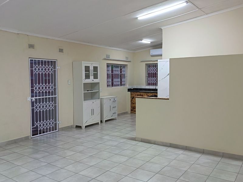 Spacious open-plan living area featuring tiled flooring, security gates, and a partial kitchen partition, offering a clean and functional layout.