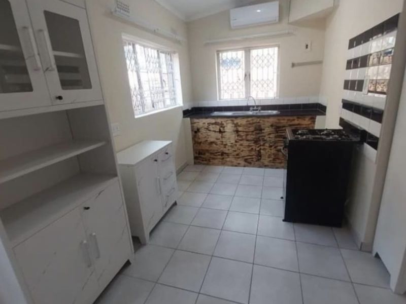 A functional kitchen featuring tiled flooring, built-in cabinetry, a double sink, and a wall-mounted air conditioning unit.
