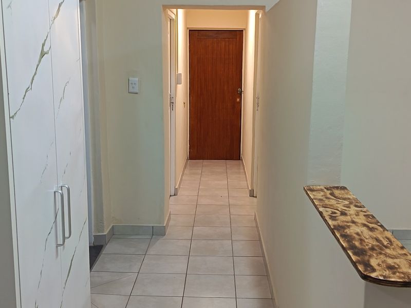 A functional hallway featuring tiled flooring, a built-in cupboard with marble-effect finish, and a solid timber door leading to an adjacent room.
