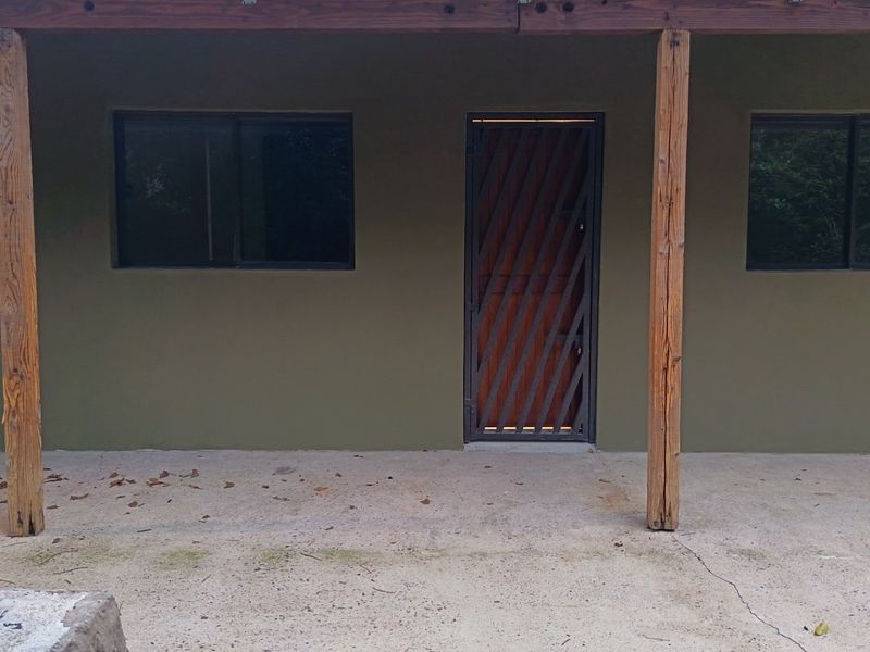 A covered patio area featuring timber support posts, concrete flooring, and a secure entrance door with sliding windows.