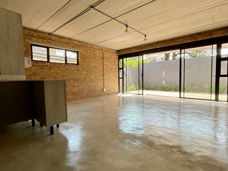 Spacious open-plan living area featuring industrial-style exposed brick walls, polished concrete floors, and large sliding glass doors leading to an outdoor space.