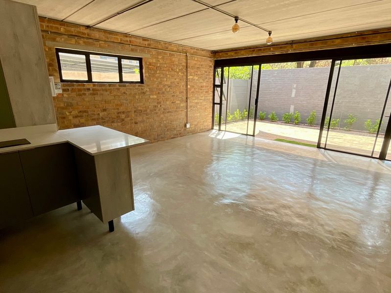 Spacious open-plan living area featuring exposed brick walls, polished concrete floors, and large sliding glass doors opening to a private outdoor space.