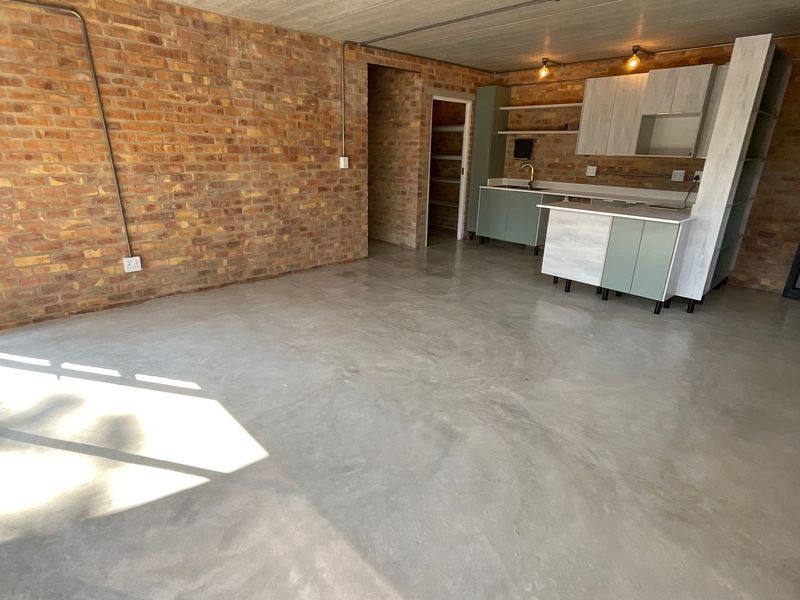 Modern open-plan living area featuring exposed brick walls, polished concrete floors, and a compact kitchen with contemporary cabinetry.