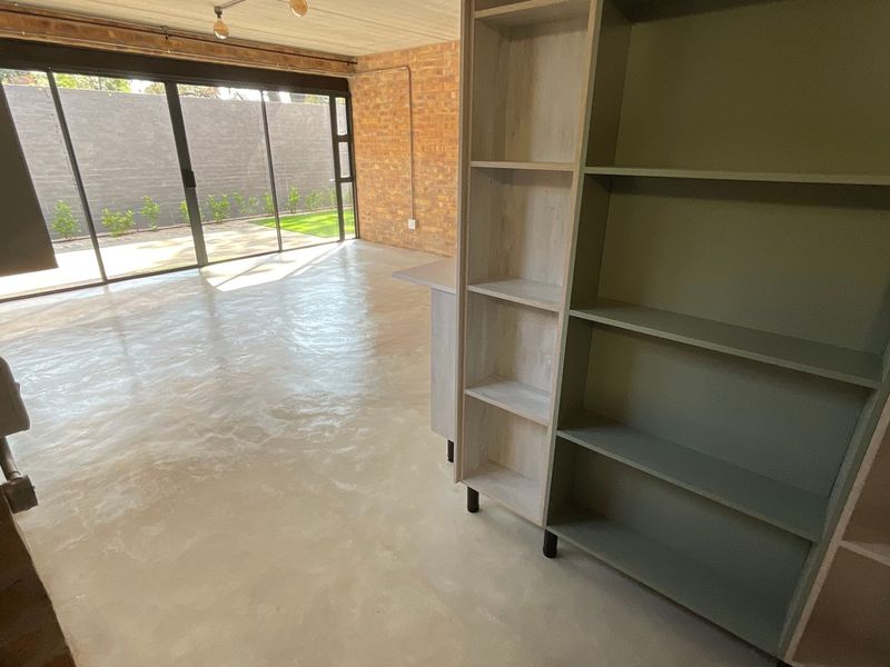 Spacious open-plan living area featuring polished concrete floors, exposed brick walls, and large sliding glass doors leading to an outdoor space.