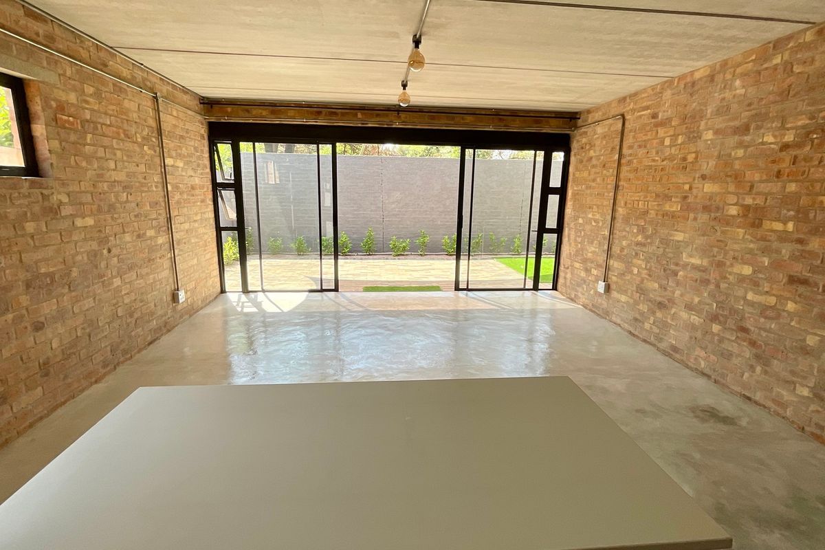 Spacious living area featuring industrial-style exposed brick walls, polished concrete floors, and large sliding glass doors opening to a private outdoor space.