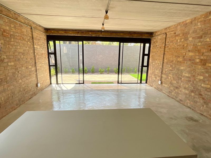 Spacious living area featuring industrial-style exposed brick walls, polished concrete floors, and large sliding glass doors opening to a private outdoor space.