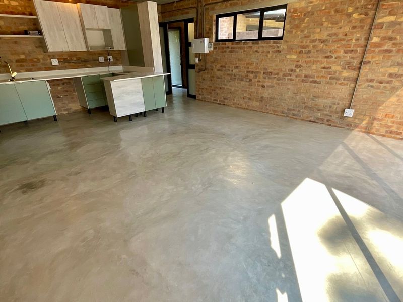 An open-plan living and kitchen area featuring industrial-style exposed brick walls, polished concrete floors, and modern fitted cabinetry with a neutral color palette.