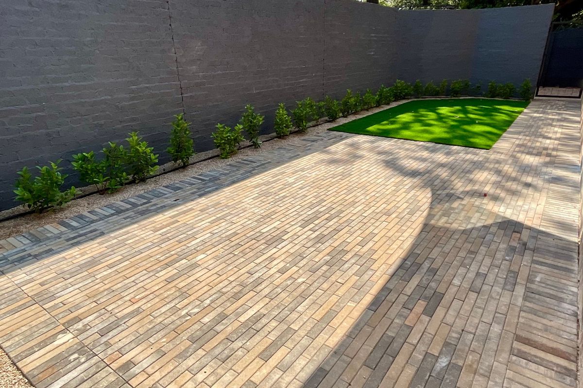 A well-maintained rear courtyard featuring neat brick paving, a section of artificial lawn, and a dark-painted boundary wall with established perimeter planting.