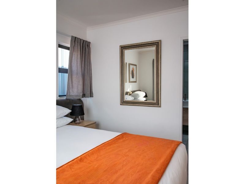 A well-maintained bedroom featuring neutral walls, a window with curtains, and an adjacent doorway leading to an en-suite bathroom.