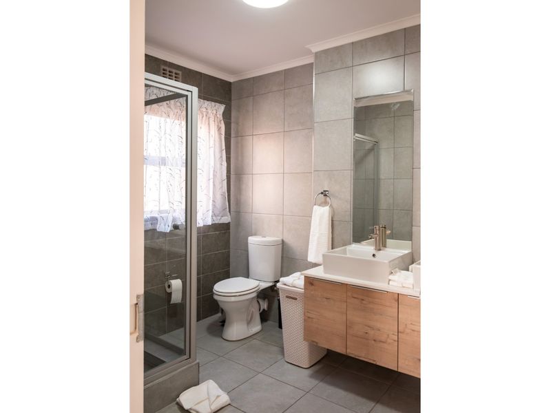 A modern bathroom featuring a glass shower enclosure, a contemporary vessel sink with a wood-finish vanity, and neutral grey wall and floor tiling.