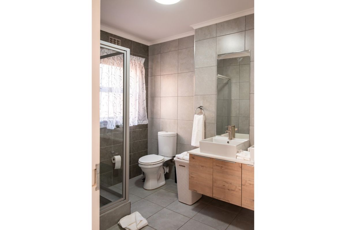 A modern bathroom featuring a glass shower enclosure, a contemporary vessel sink with a wood-finish vanity, and neutral grey wall and floor tiling.