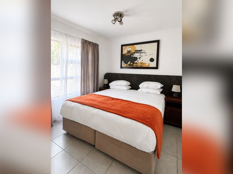 A well-maintained bedroom featuring neutral tiled flooring, a large window for natural light, and a modern ceiling-mounted spotlight fixture.