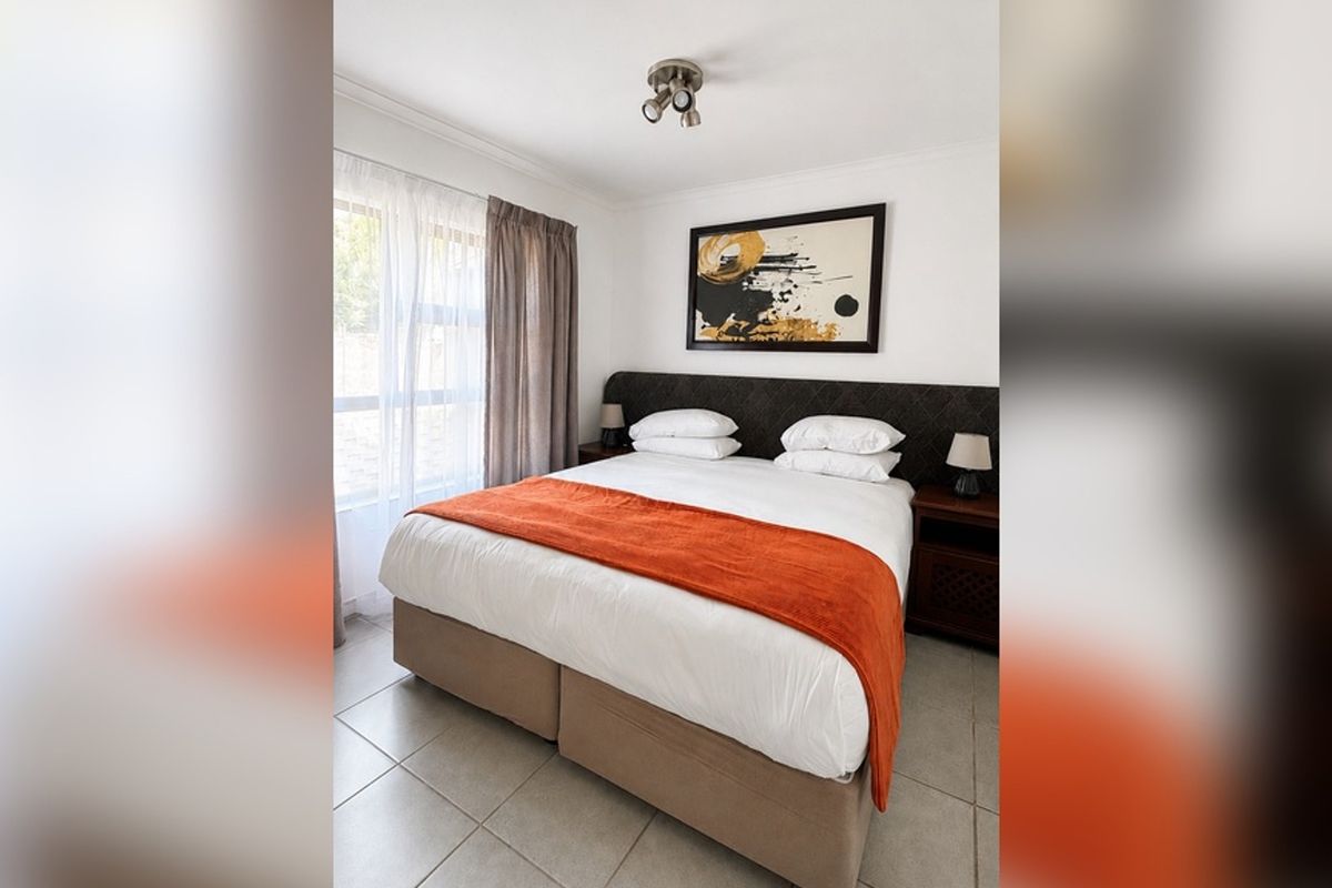 A well-maintained bedroom featuring neutral tiled flooring, a large window for natural light, and a modern ceiling-mounted spotlight fixture.