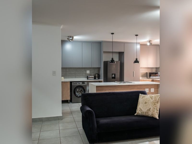 Modern open-plan kitchen and living area featuring contemporary cabinetry, a central island, tiled flooring, and integrated laundry facilities.