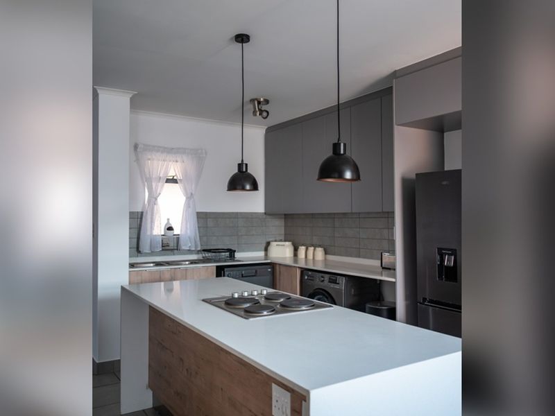 Modern kitchen featuring a central island with a built-in hob, sleek grey cabinetry, stone countertops, and a stylish subway tile backsplash.