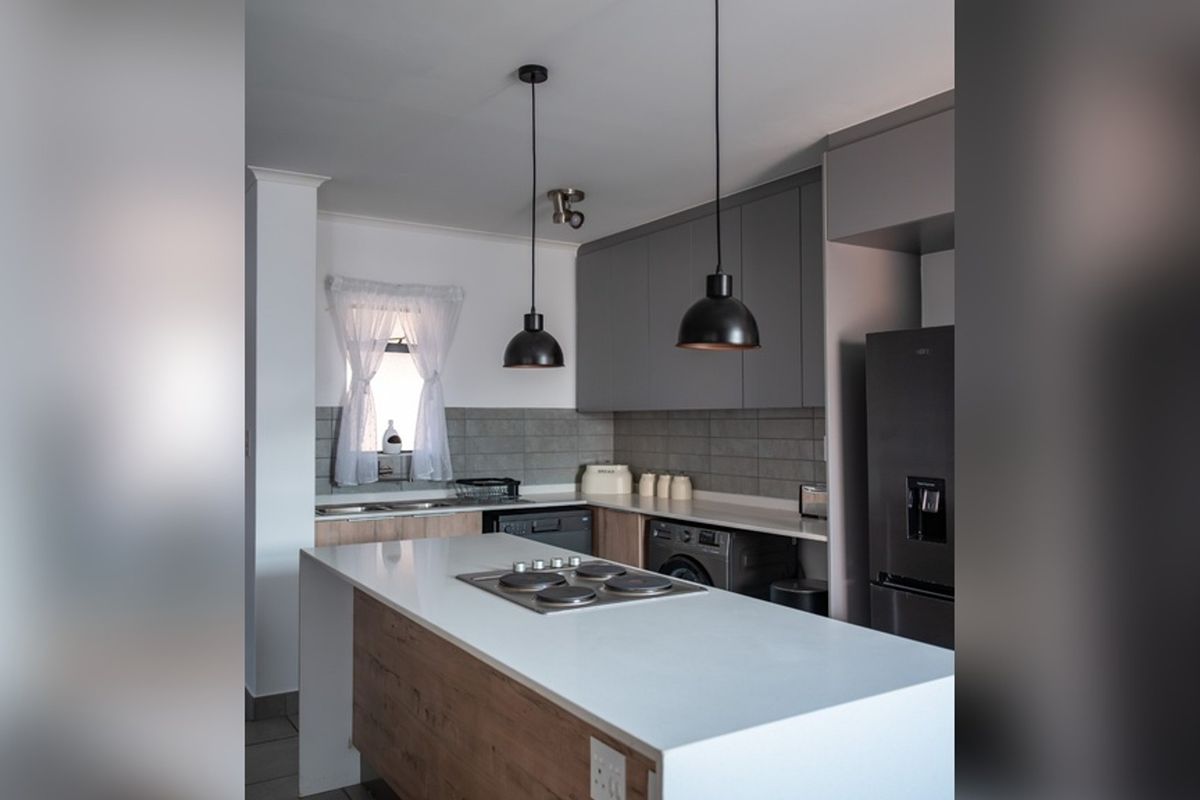 Modern kitchen featuring a central island with a built-in hob, sleek grey cabinetry, stone countertops, and a stylish subway tile backsplash.