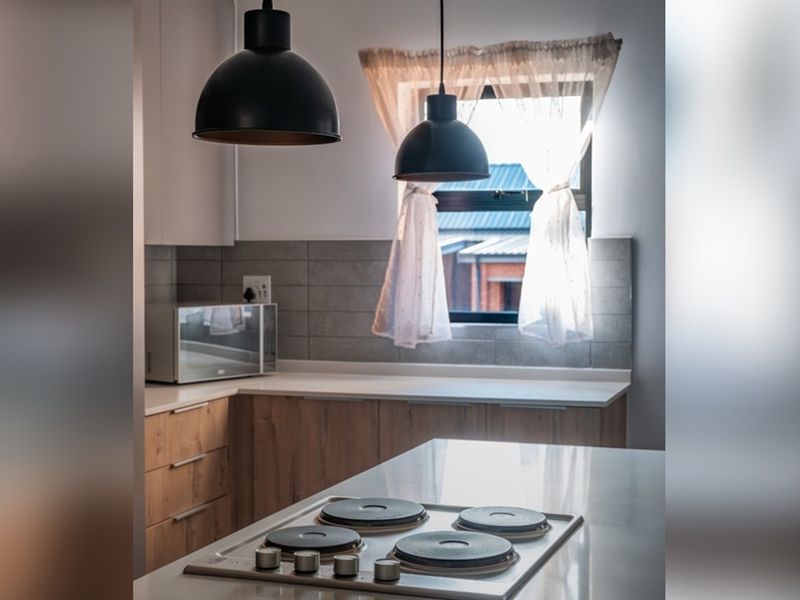 Modern kitchen featuring light wood cabinetry, stone countertops, a built-in electric hob, and stylish pendant lighting with a tiled backsplash.