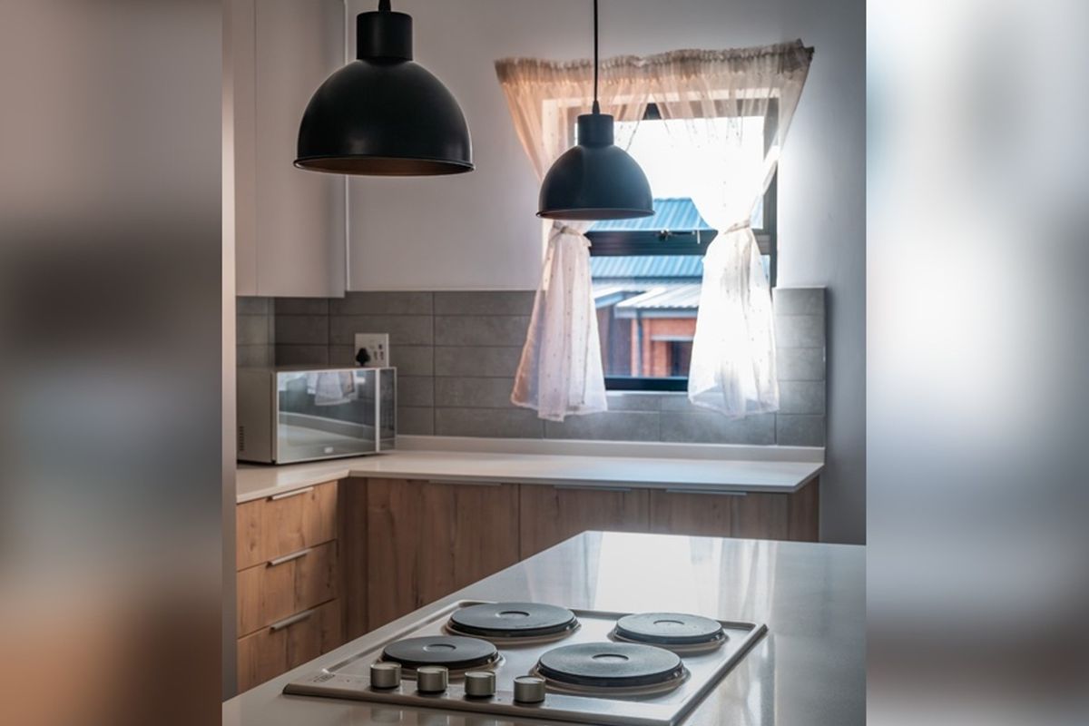 Modern kitchen featuring light wood cabinetry, stone countertops, a built-in electric hob, and stylish pendant lighting with a tiled backsplash.