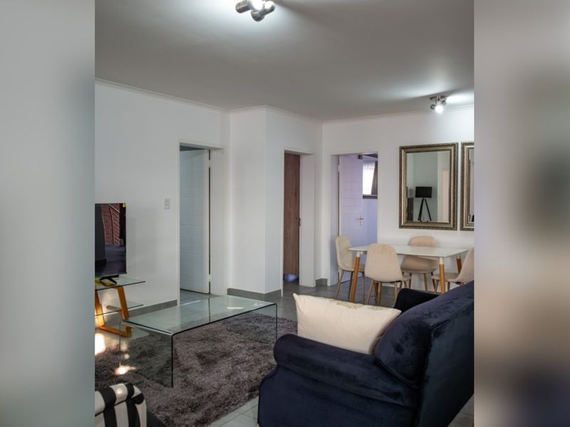 An open-plan living and dining area featuring neutral walls, tiled flooring, and multiple access points to other rooms within the apartment.