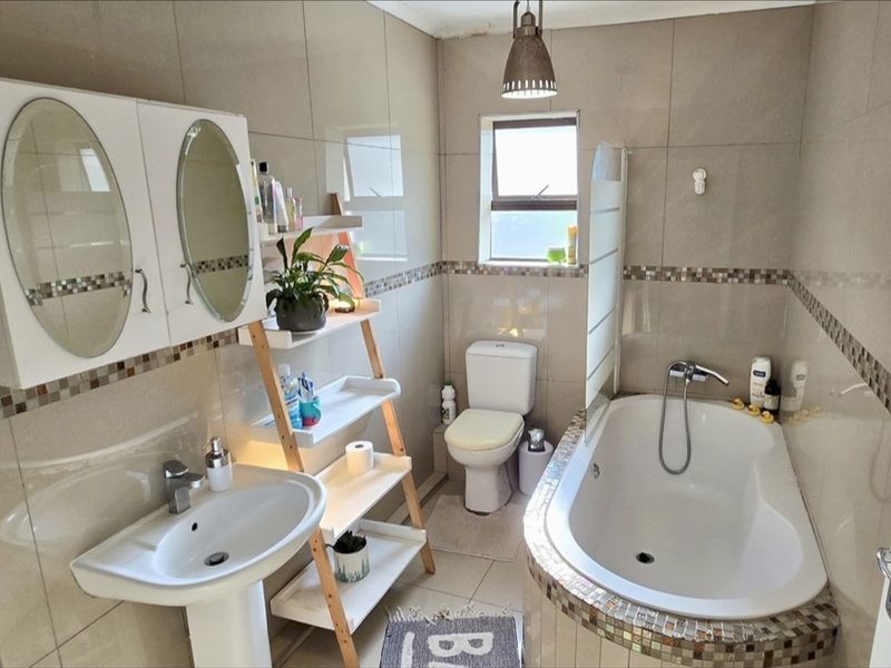 A well-maintained bathroom featuring a pedestal basin, a built-in bathtub with a glass screen, a toilet, and neutral wall and floor tiling.