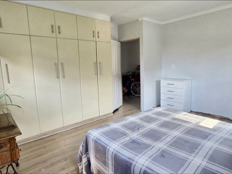 A bedroom featuring extensive built-in cupboards, laminate flooring, and coved ceilings, offering a functional space with potential for cosmetic updates.