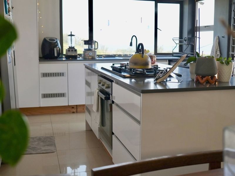 Modern kitchen featuring a central island with a built-in oven and gas hob, complemented by sleek cabinetry, stone countertops, and large windows.