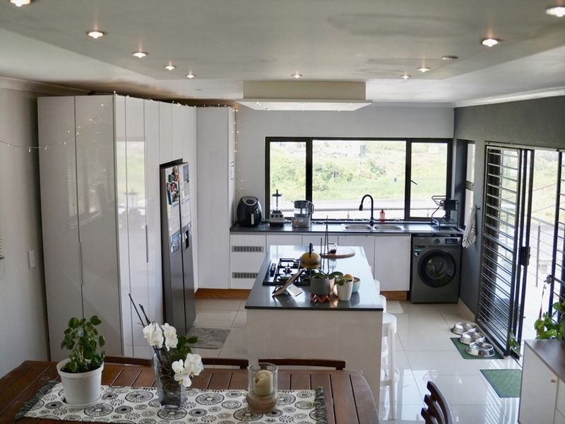 Modern kitchen featuring high-gloss cabinetry, a central island with a gas hob, integrated appliances, and large windows providing ample natural light.