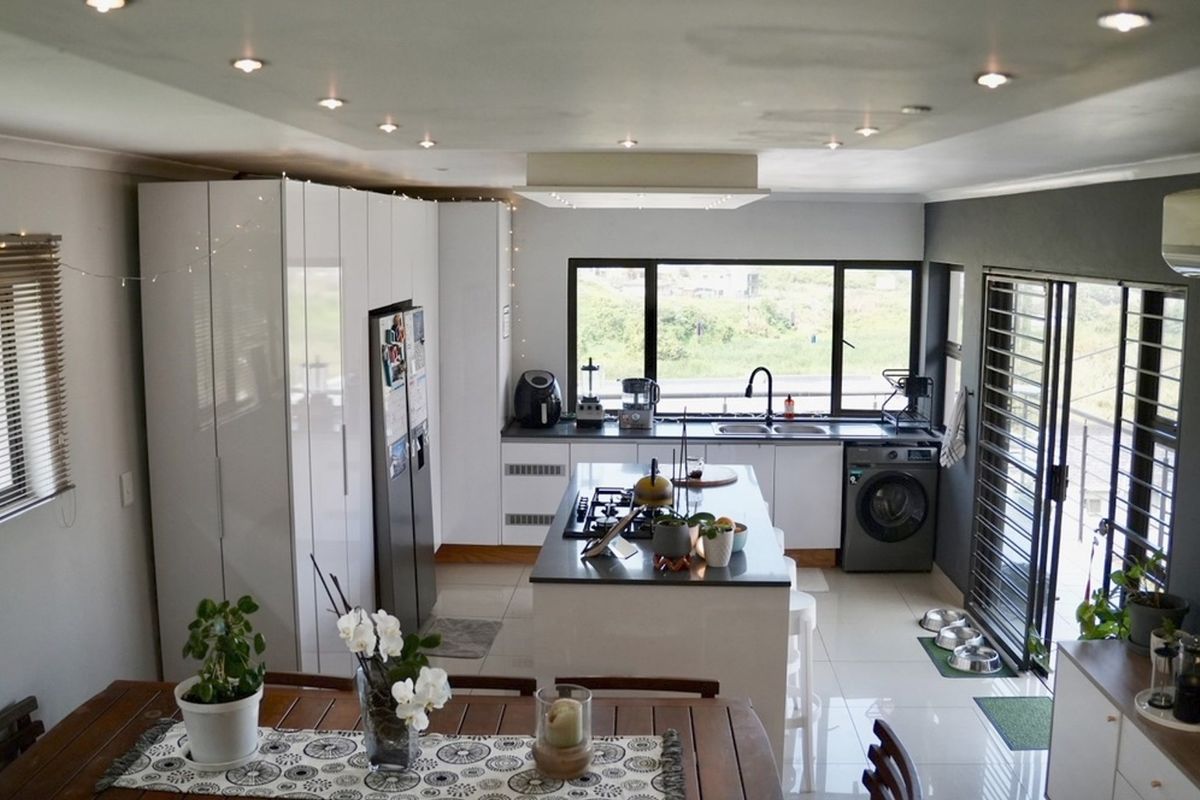 Modern kitchen featuring high-gloss cabinetry, a central island with a gas hob, integrated appliances, and large windows providing ample natural light.