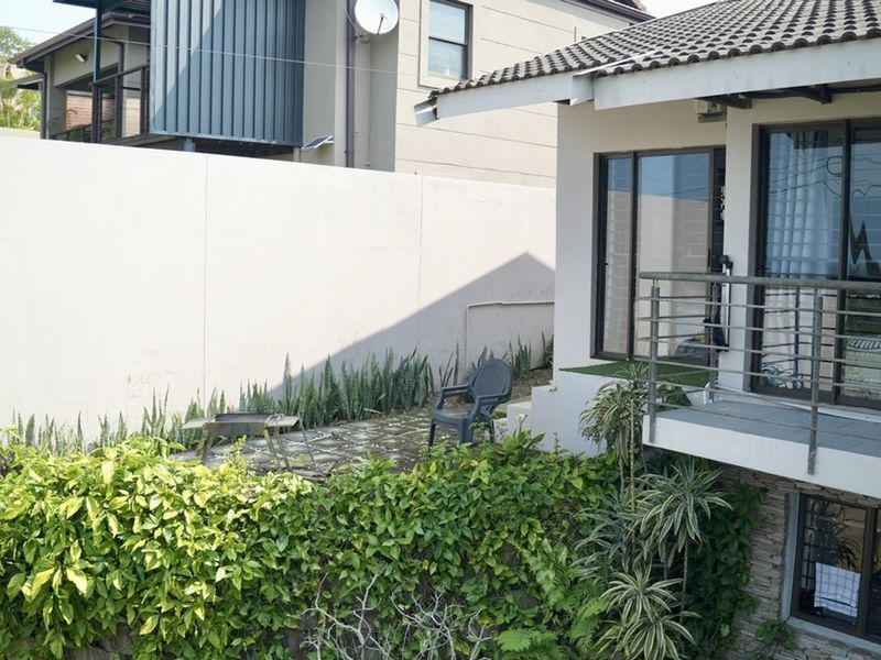 Rear exterior view featuring a balcony with metal railings, a paved patio area, and a high boundary wall with established garden greenery.
