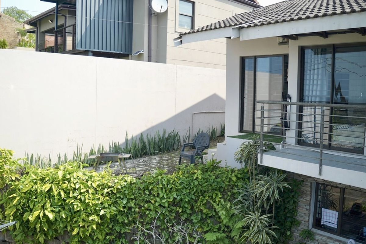 Rear exterior view featuring a balcony with metal railings, a paved patio area, and a high boundary wall with established garden greenery.