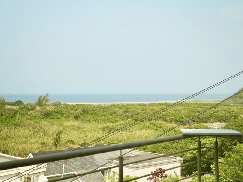 Elevated coastal view overlooking lush green vegetation and the ocean, framed by a metal balcony railing.