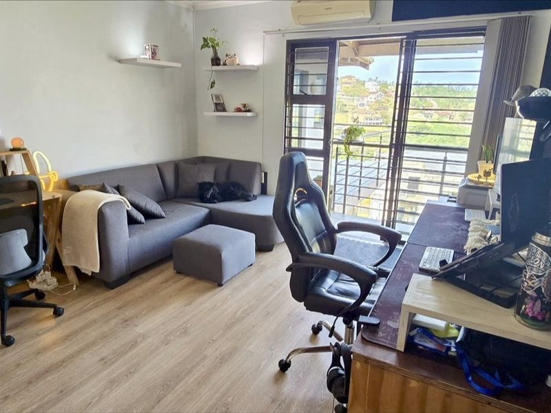A functional living room featuring laminate flooring, wall-mounted air conditioning, and a sliding glass door providing access to a balcony with scenic views.