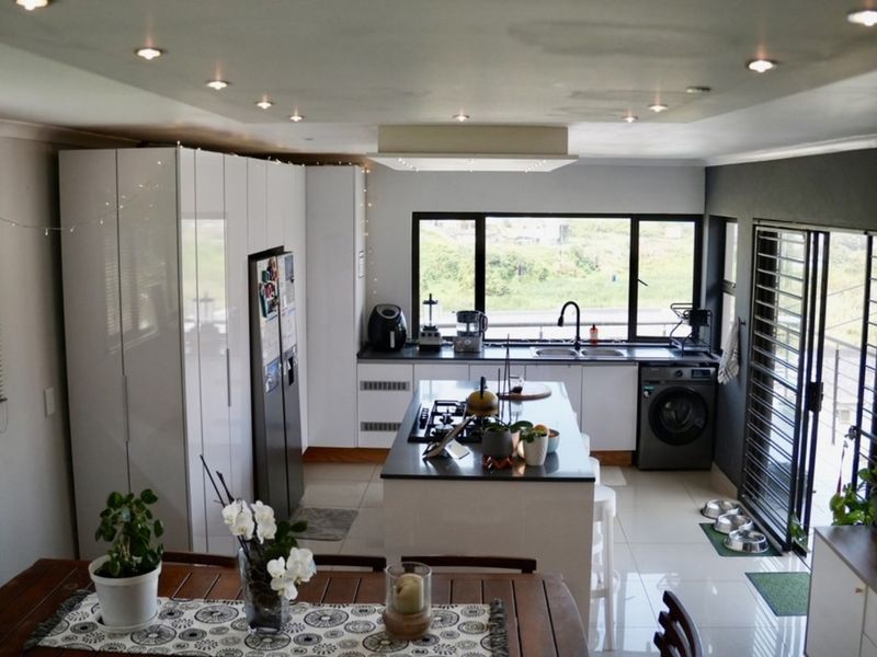 Modern open-plan kitchen featuring a central island with gas hob, sleek white cabinetry, integrated appliances, and large windows providing ample natural light.