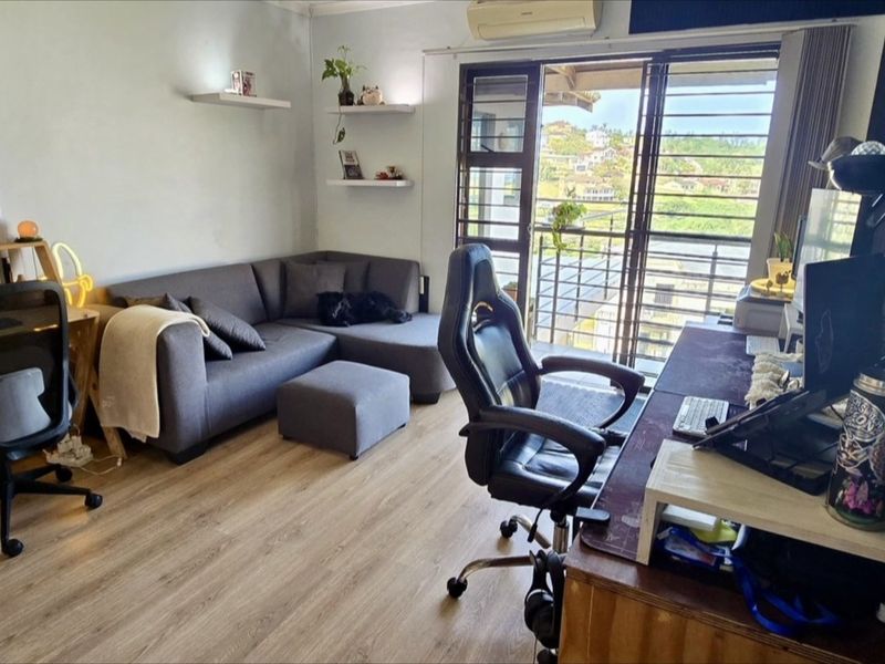 A functional living area featuring laminate flooring, wall-mounted air conditioning, and a sliding glass door providing access to a balcony with exterior views.