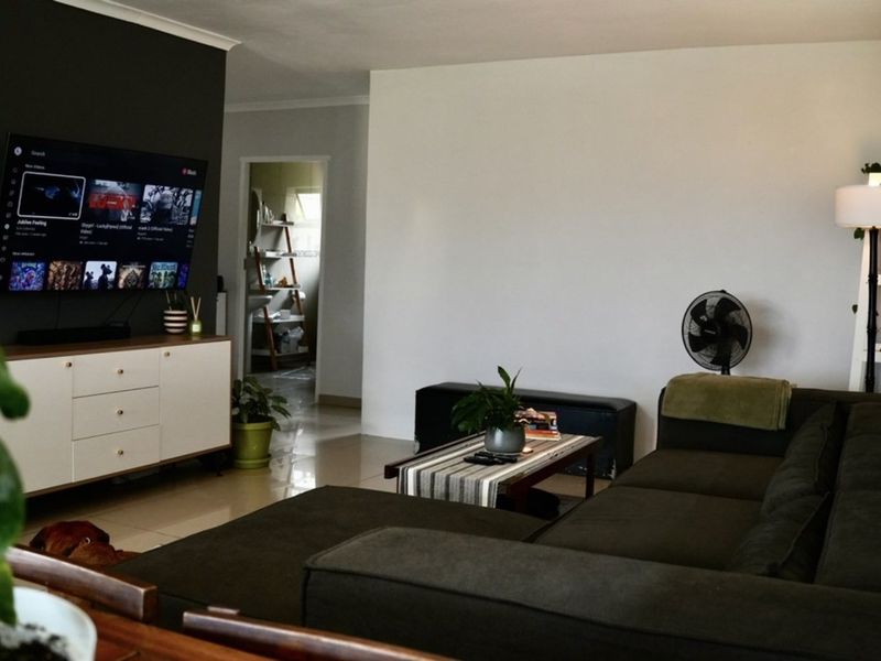 A well-maintained living room featuring tiled flooring, a dark accent wall, and a wall-mounted television, providing a comfortable and functional living space.