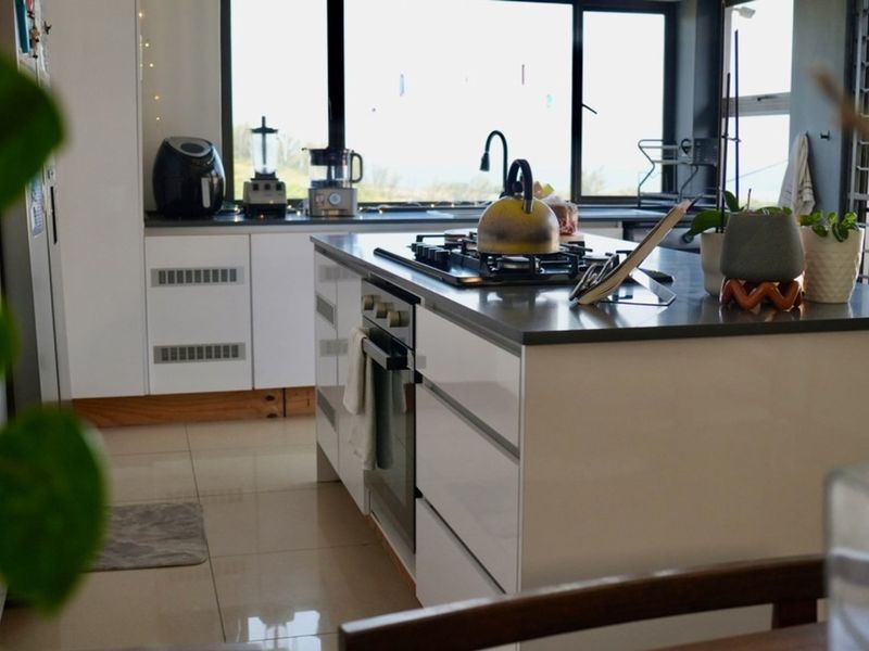 Modern kitchen featuring a central island with a built-in oven and gas hob, complemented by sleek cabinetry and large windows providing natural light.